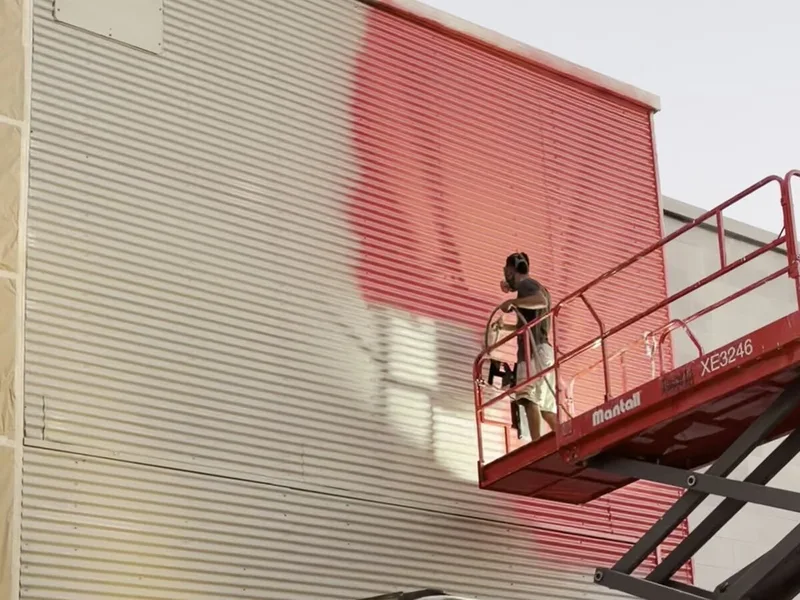 צובע מתיז צבע על חזית חנות מבמה מרימה